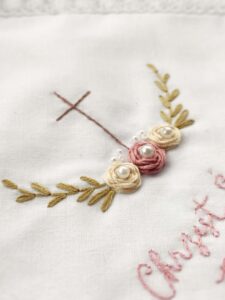 biała szatka z motywem krzyża i różyczek z perełkami i haftowanym imieniem dziecka oraz datą chrztu
