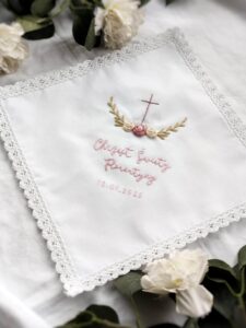 biała szatka z motywem krzyża i różyczek z perełkami i haftowanym imieniem dziecka oraz datą chrztu
