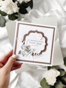 Elegancka kartka na rocznicę ślubu z imionami jubilatów i papierowymi kwiatami oraz serduszkami