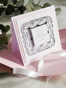 Pastelowo różowa kartka ze srebrną ażurową ramką i personalizacją na ślub