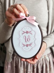 Owalny haftowany obrazek z inicjałem i kwiatami