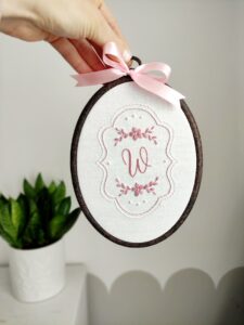 Owalny haftowany obrazek z inicjałem i kwiatami