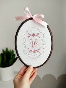 Owalny haftowany obrazek z monogramem i kwiatami