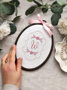 Owalny haftowany obrazek z monogramem i kwiatami