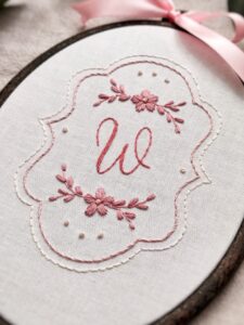 Owalny haftowany obrazek z inicjałem i kwiatami
